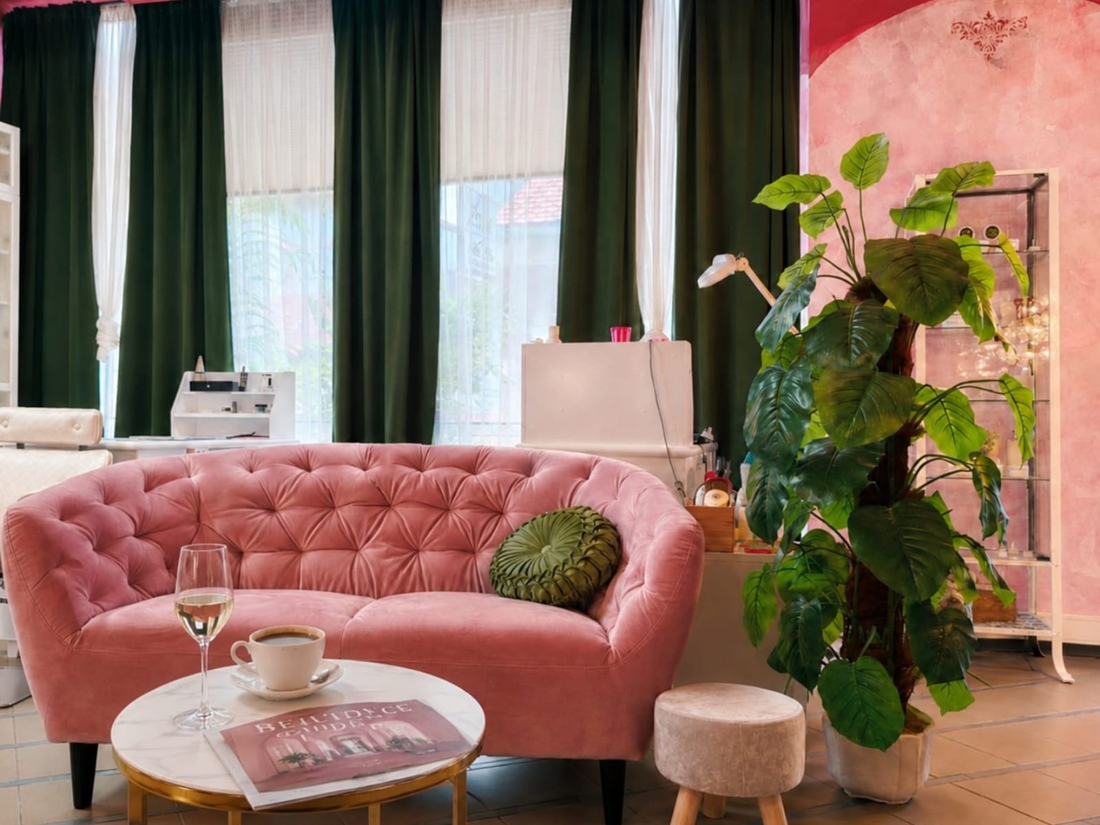 Wartebereich mit rosa Samtsofa, grüner Pflanze und hohen Fenstern